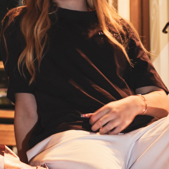 Woman sitting outside shops at night with a pink bag wearing be better pink track pants and a heavy Plum Purple tee with Dusty Pink Embroirered Be Better logos